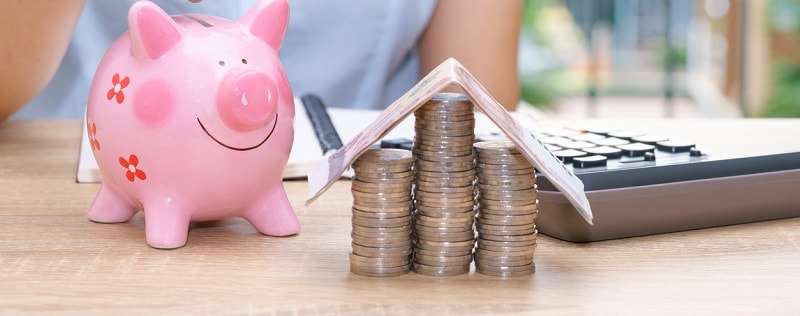 Main d’une femme mettant une pièce dans une tirelire rose sur un bureau en bois - économisé de l'argent pour acheter le concept de maison.