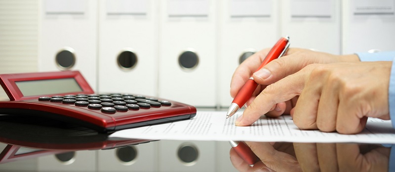 Une personne vérifiant les termes d'un contrat à l'aide d'une calculatrice et une loupe à la main