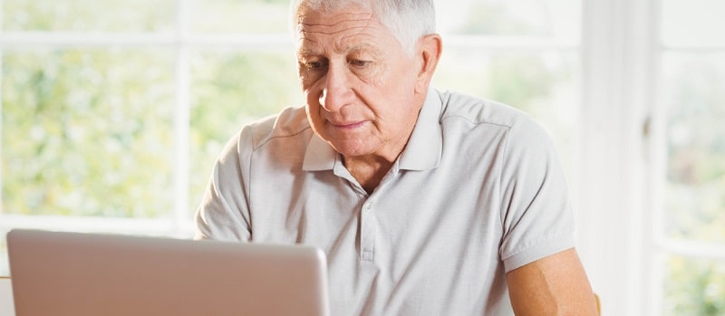 un senior devant un laptop,avec des documents à la main