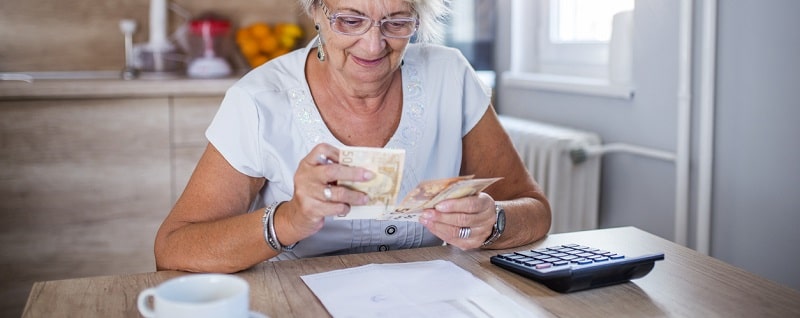 Heureuse femme senior avec calculatrice et factures comptant de l'argent en euros à la maison.