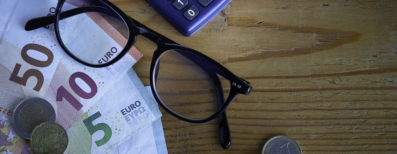 Composition avec billets de banque et pièces (Euros), paire de lunettes et calculatrice sur fond en bois