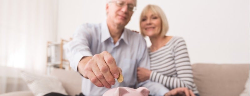 Un couple de personnes âgées met de la monnaie dans la tirelire, économisant de l’argent à la maison.