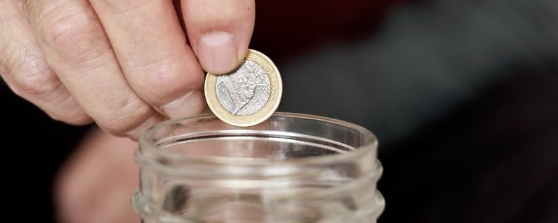 Gros plan d’un vieil homme caucasien sauvant une pièce d’un euro dans un pot de verre.