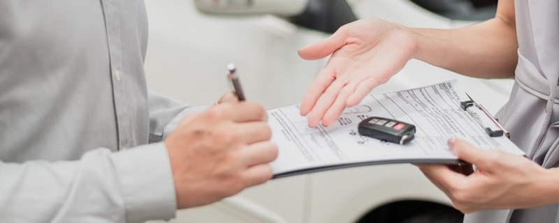Un client heureux et un agent d’assurance automobile concluent un accord et signent un contrat dans un showroom automobile.
