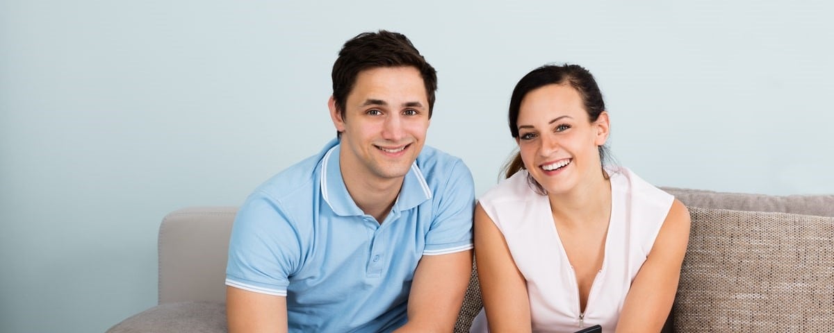 Jeune couple heureux assis sur un canapé calculant son budget à la maison.