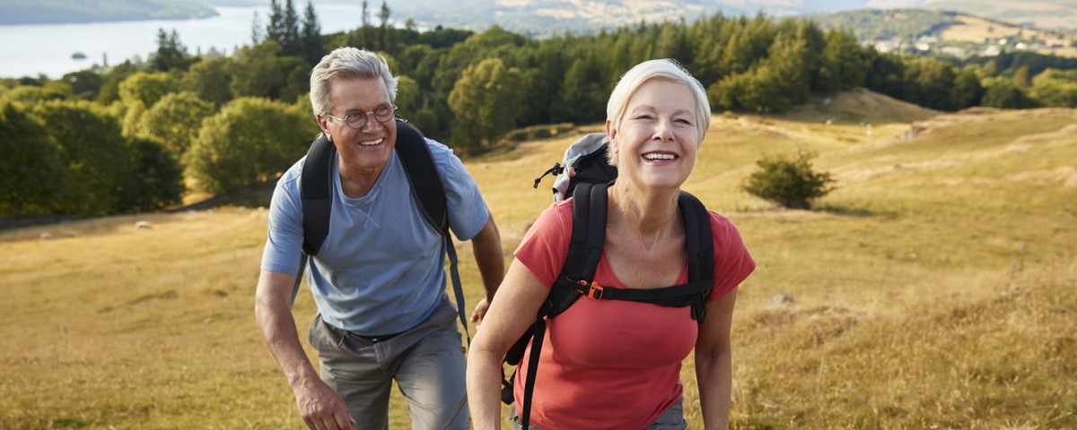 Portrait d'un couple de seniors grimpant une colline lors d'une randonnée à travers la campagne.