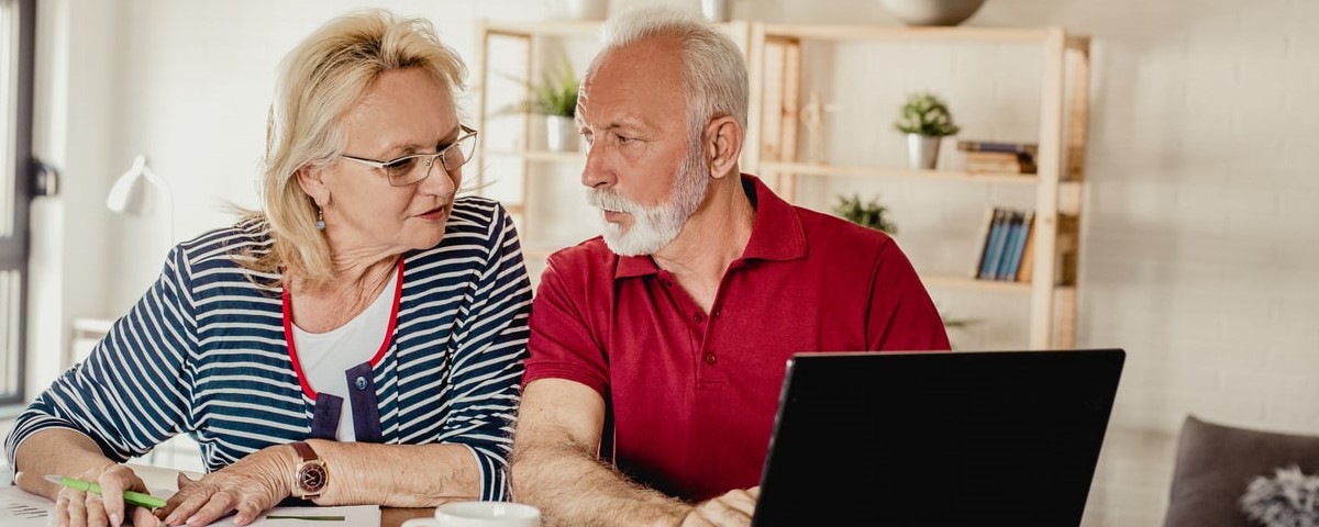 Un couple d'aînés est à la table, utilisant un ordinateur portable et ils planifient ensemble un budget familial.