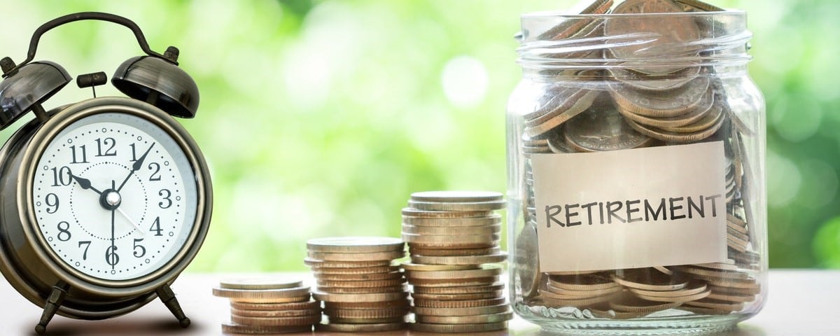 Main mettant des pièces de monnaie dans un bocal en verre avec un réveil rétro pour le concept d'épargne-retraite.