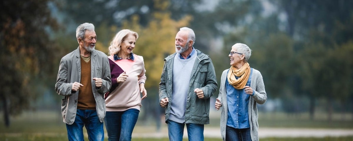 Groupe de personnes âgées heureuses communiquant tout en courant dans un parc en automne.