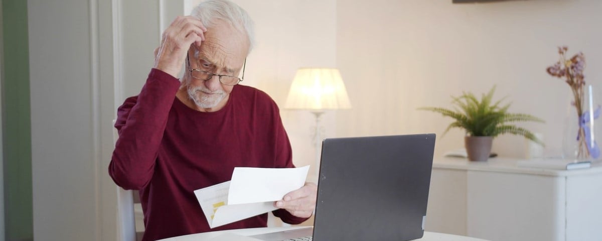 Photo recadré d'un homme âgé passant en revue ses finances, assis sur le canapé de sa maison.