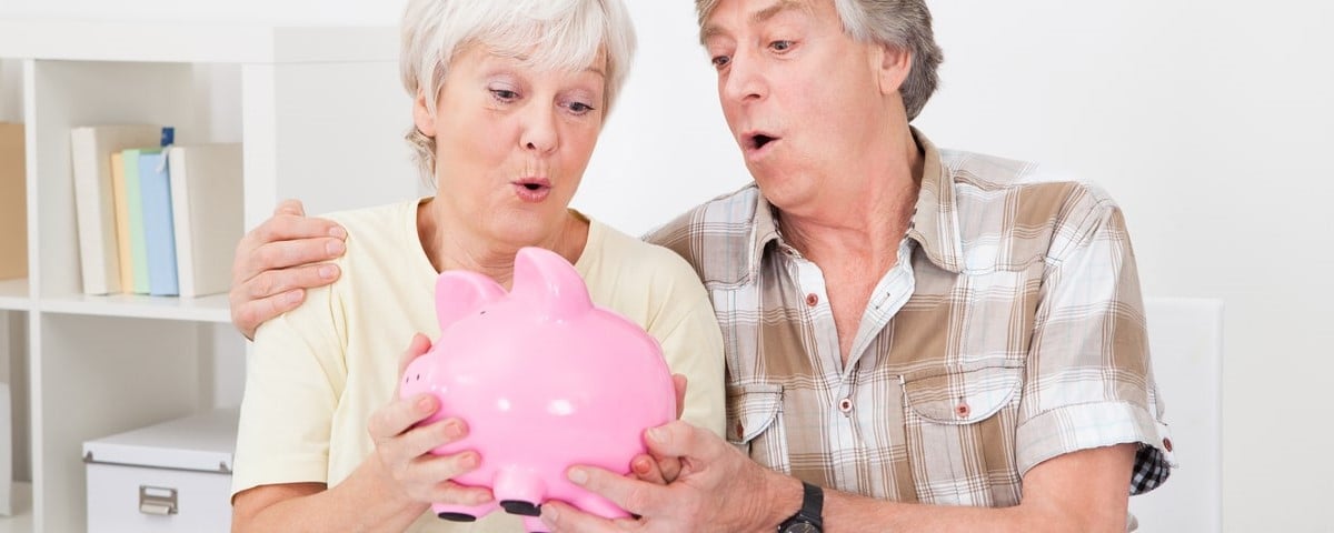 Portrait d'un couple de seniors économisant de l'argent dans une tirelire rose