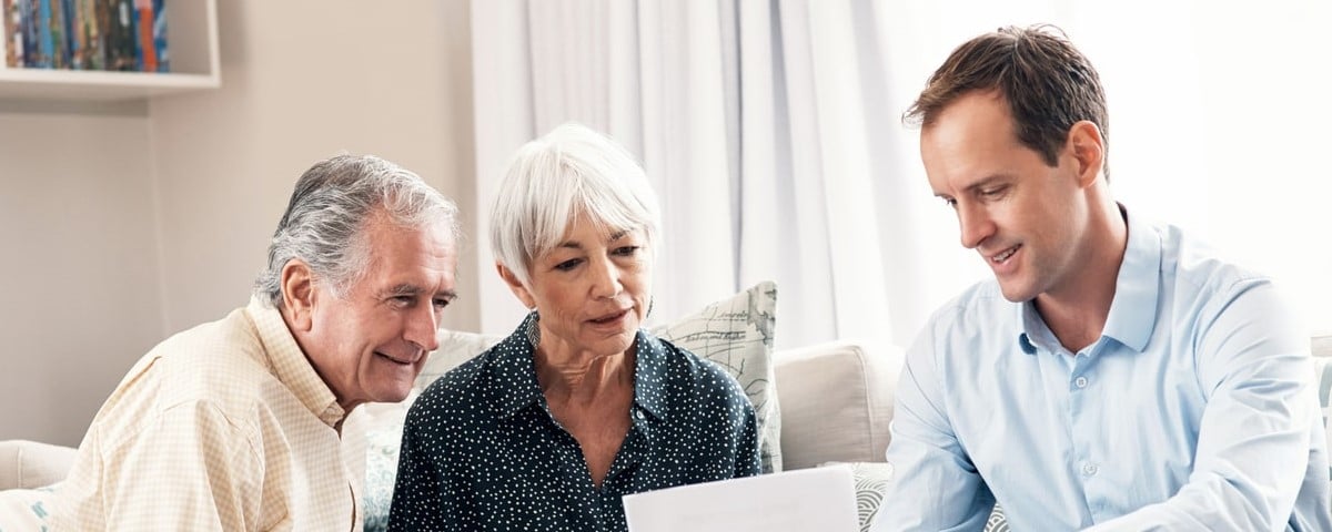 Vue d'un couple de personnes âgées recevant les conseils de leur conseiller financier à domicile