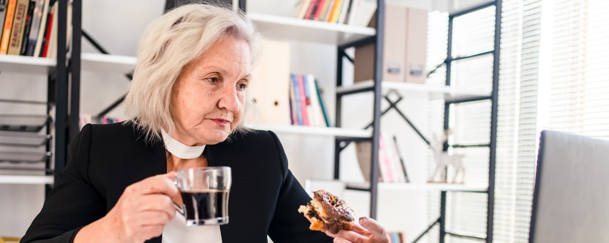 femme âgée mangeant un beignet pendant sa pause