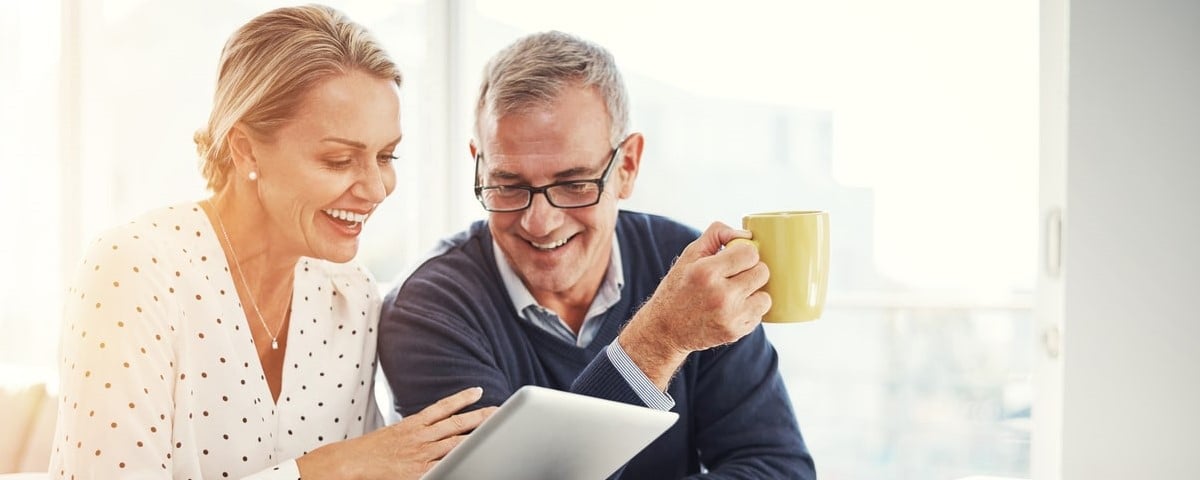 Photo d'un couple d'âge mûr utilisant une tablette numérique tout en examinant des documents financiers à la maison.