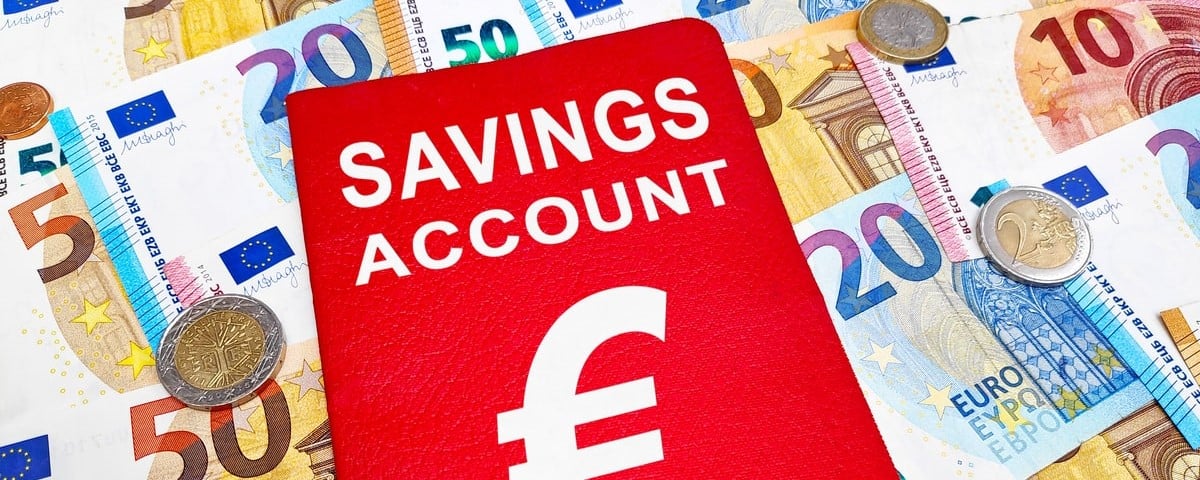 Livret de compte d'épargne au-dessus d'une pile de billets et de pièces en euros.