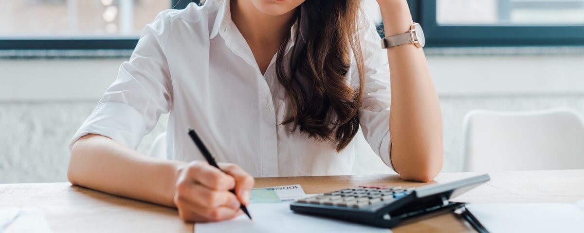 Femme d'affaires frustrée signant un document près d'une calculatrice.