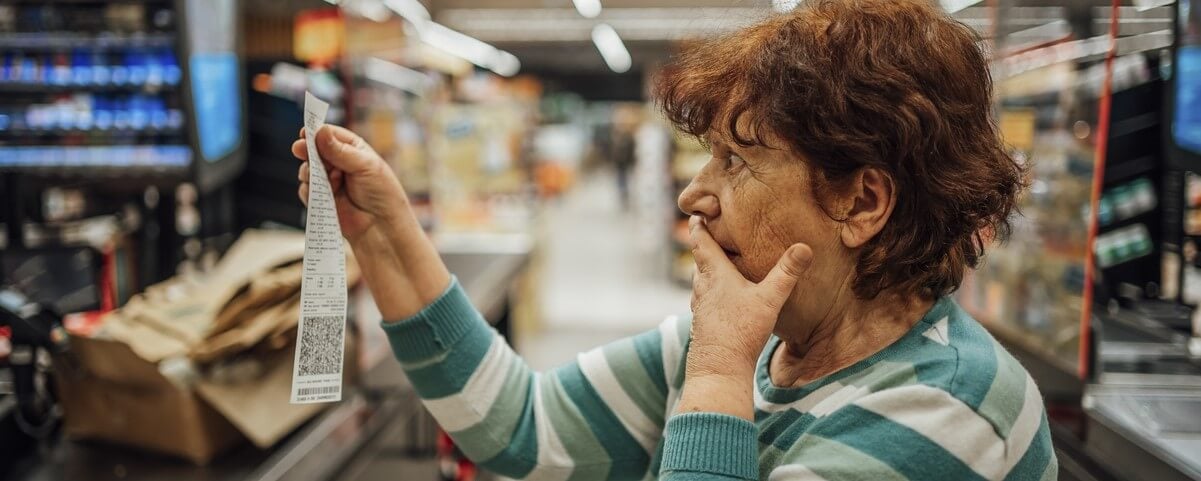 Une femme âgée est choquée par le montant élevé de la facture au supermarché.