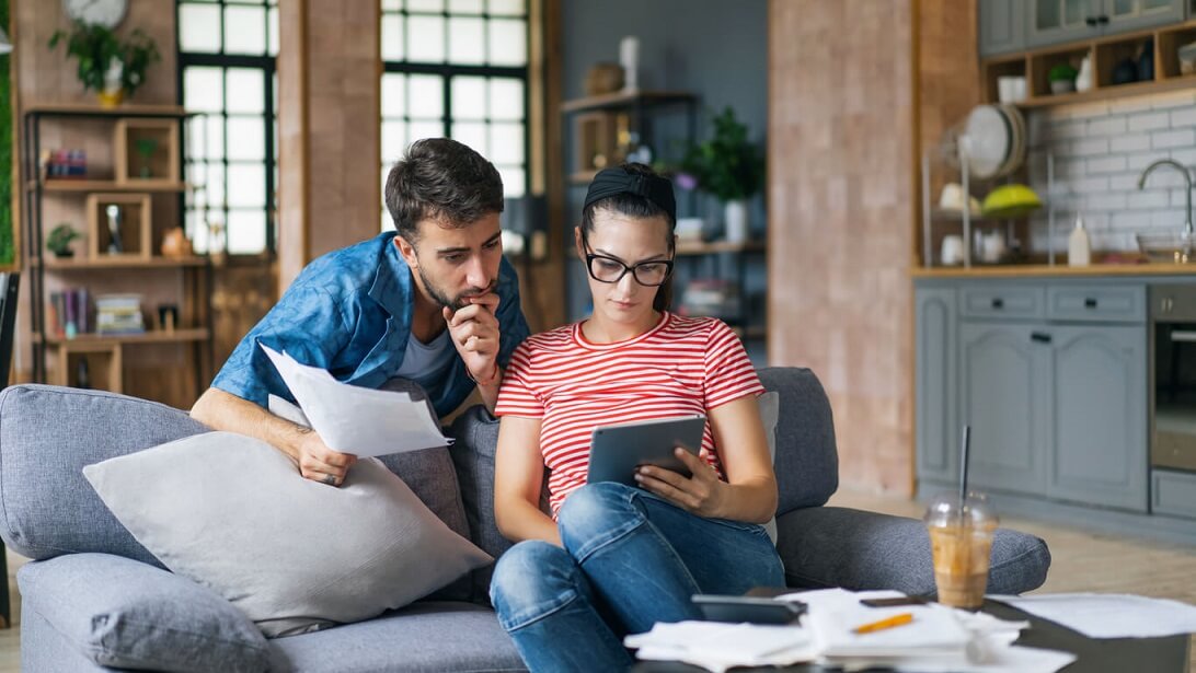 Un couple calcule des factures à la maison à l'aide d'un ordinateur portable et d'une calculatrice.