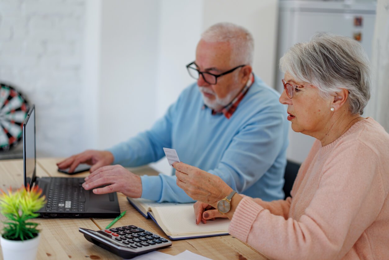 Femme âgée détenant une carte de crédit et utilisant un ordinateur portable tout en payant des factures à la maison avec une carte de crédit