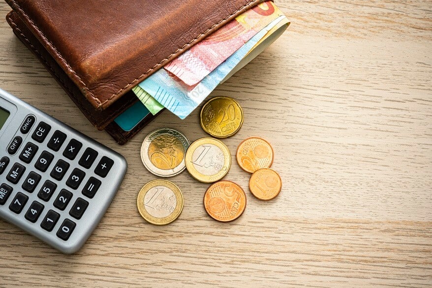 Vue aérienne de billets de banque et de pièces en euros sortant d'un portefeuille et d'une calculatrice de poche bruns.