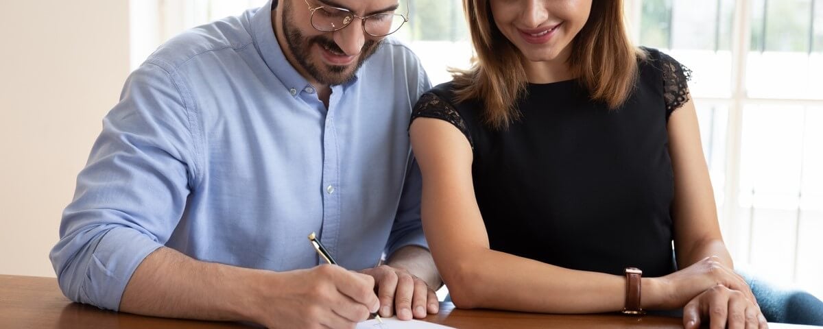 Couple souriant apposant sa signature sur des documents.