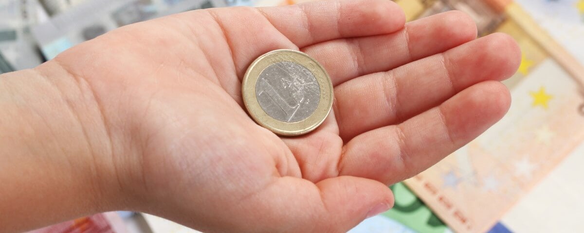 Pièce d'un euro sur la main d'un enfant sur fond de billets de banque en euros