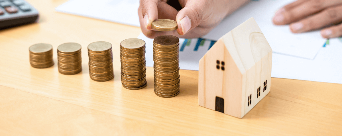 Homme d'affaires plaçant des pièces de monnaie sur des piles de pièces de monnaie avec un modèle de maison tout en se préparant à épargner pour un investissement immobilier et un prêt hypothécaire.
