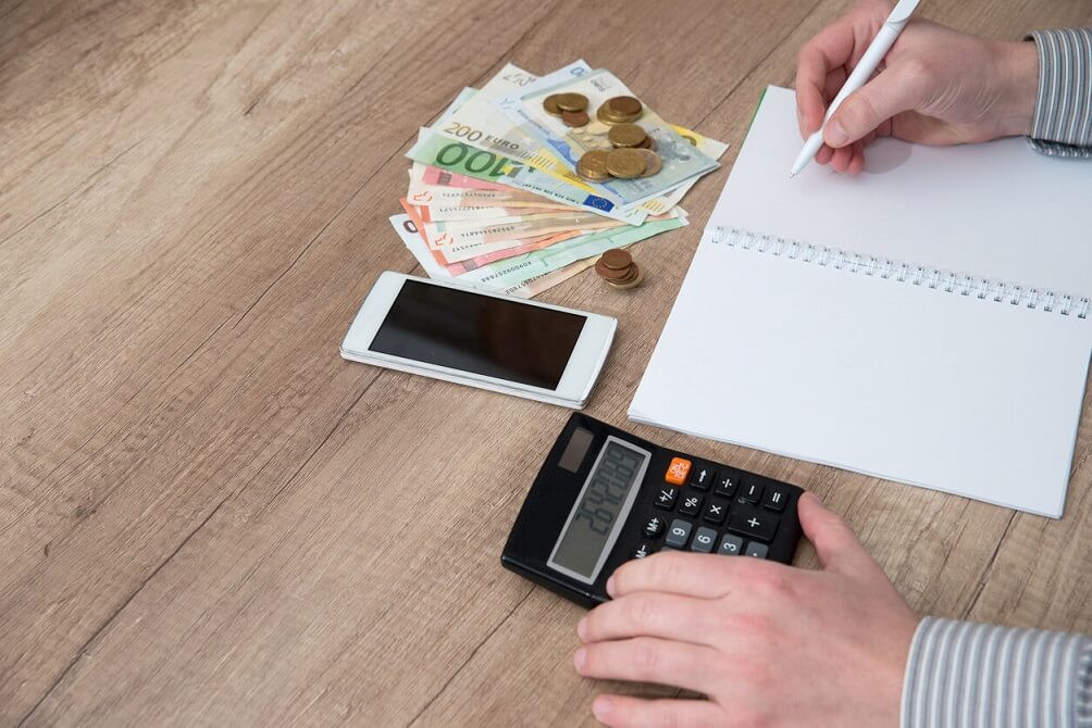 Main d'homme écrivant dans un agenda d'affaires stylo plume avec calculatrice, argent en euros.