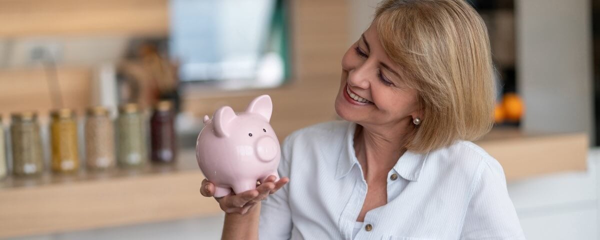 Portrait d'une femme adulte à la maison économisant de l'argent dans une tirelire et ayant l'air heureuse â home finances concepts.