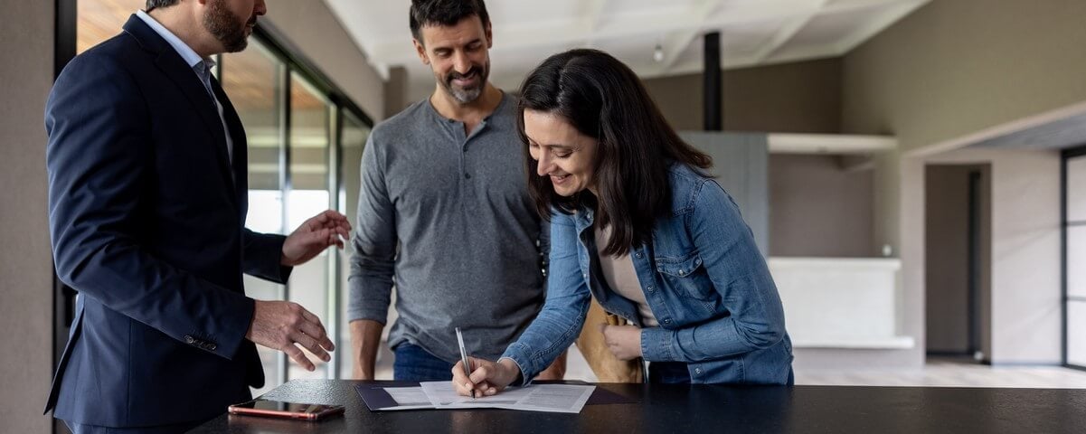 Heureux couple achetant une maison et signant l'acte devant leur agent immobilier - concepts d'accession à la propriété.
