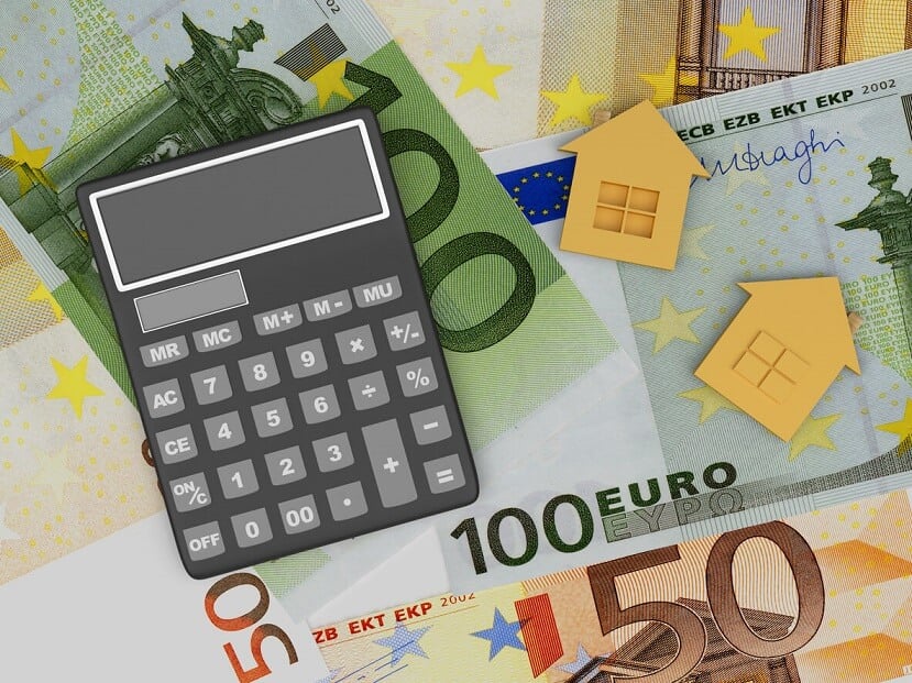 Calculatrice sur un tas de billets de banque en euros et d'icônes de maisons en or.