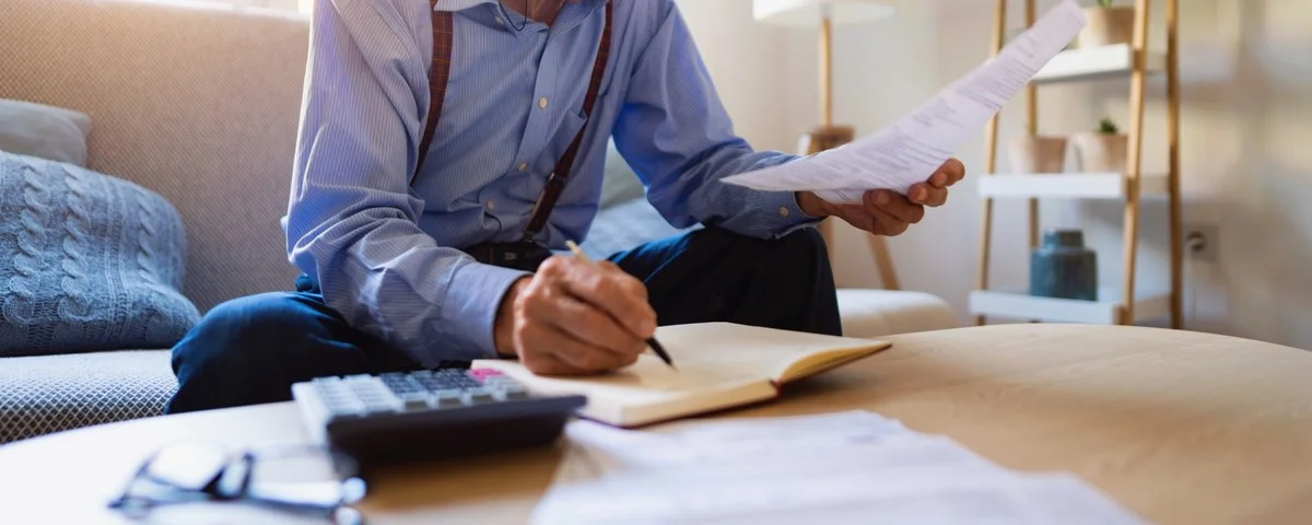 Vue en contre-plongée d'un homme âgé de type caucasien en train d'examiner ses finances à la maison et d'analyser des factures tout en écrivant dans un agenda.