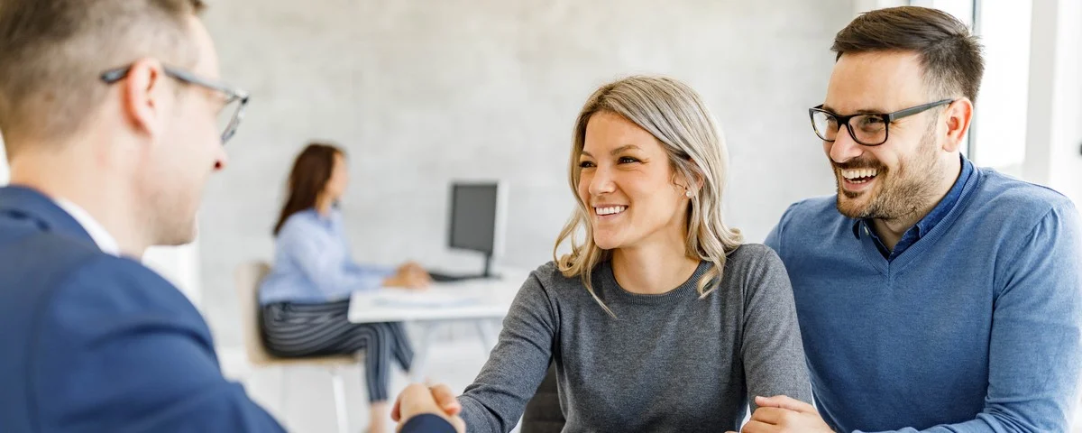 Un jeune couple heureux a conclu un accord avec son agent d'assurance lors d'une réunion au bureau.