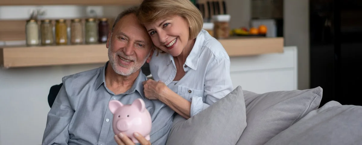 Portrait d'un couple de seniors à la maison épargnant pour leur pension dans une tirelire et regardant l'appareil photo en souriant â home finances concepts.