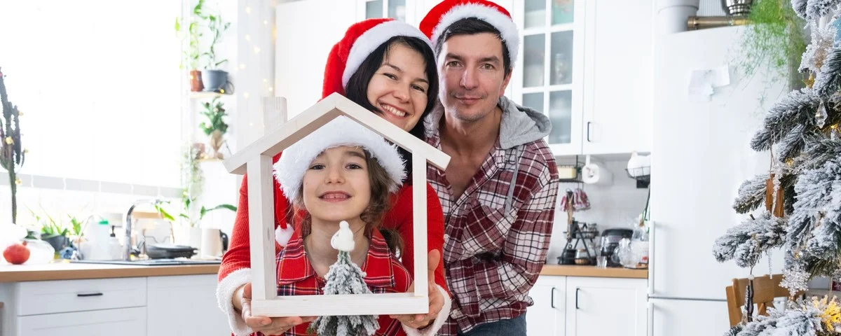 La famille heureuse dans les bonnets du père Noël avec la petite maison dans la maison confortable avec la décoration de Noël de la cuisine festive blanche.