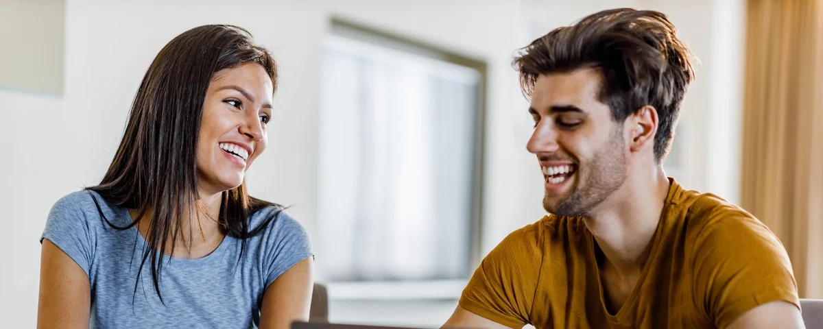 Jeune couple heureux communiquant tout en payant ses factures sur son ordinateur portable à la maison.