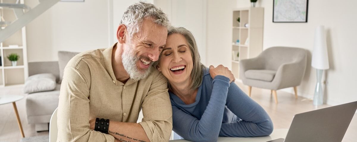 Un couple âgés de 50 ans et plus, s'amusent et sont satisfaits de l'achat d'une assurance et du paiement des factures en ligne.