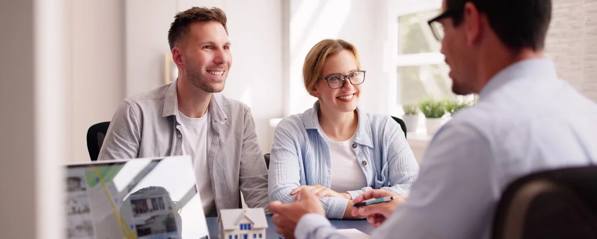 Architecte d'entreprise présentant des plans de rénovation à un jeune couple sur ordinateur portable dans un bureau, discutant d'un projet de maison familiale avec un agent immobilier.