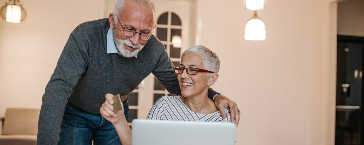 Un couple de personnes âgées est en train d'examiner des documents d'assurance en ligne sur un ordinateur portable.