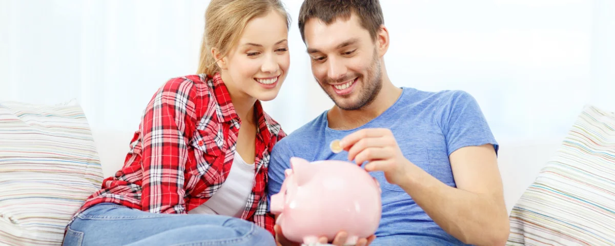 Jeune couple souriant avec une tirelire assis sur un canapé.