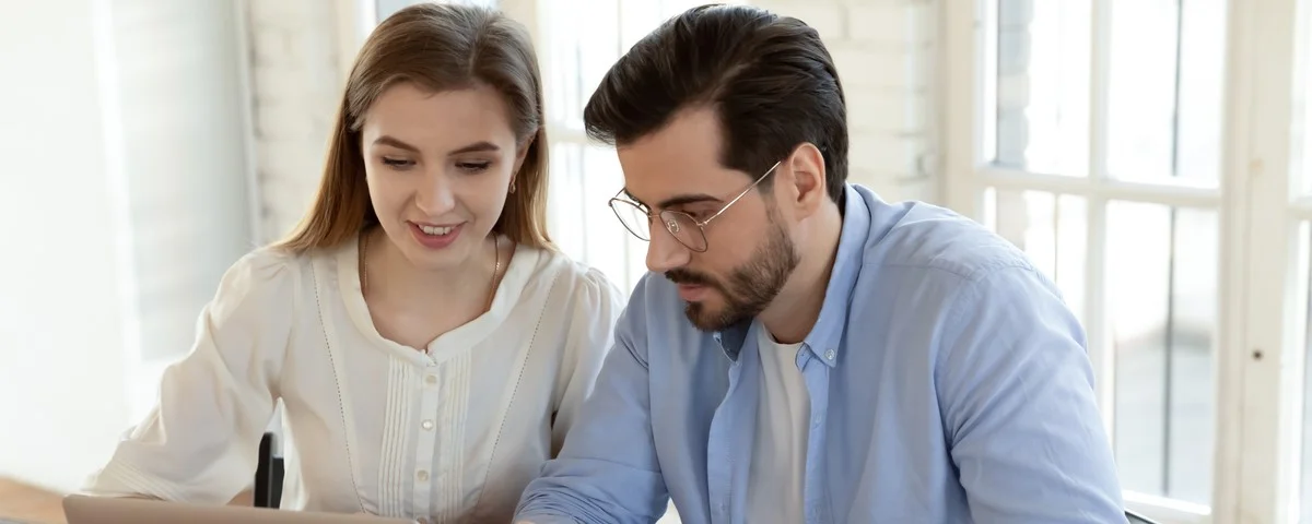 La femme cadre millénaire positive et sympathique aide un collègue masculin concentré à trouver des informations en ligne.