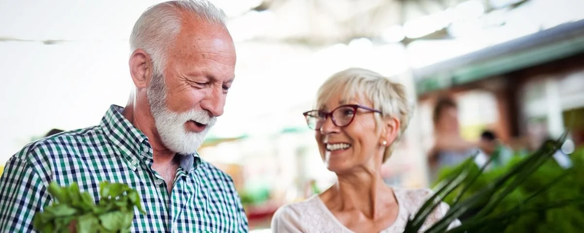 Couple de seniors souriants tenant un panier de légumes à l'épicerie