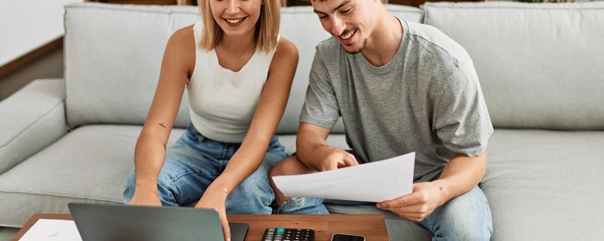 Jeune couple caucasien souriant, heureux de contrôler l'économie familiale en utilisant un ordinateur portable à la maison.