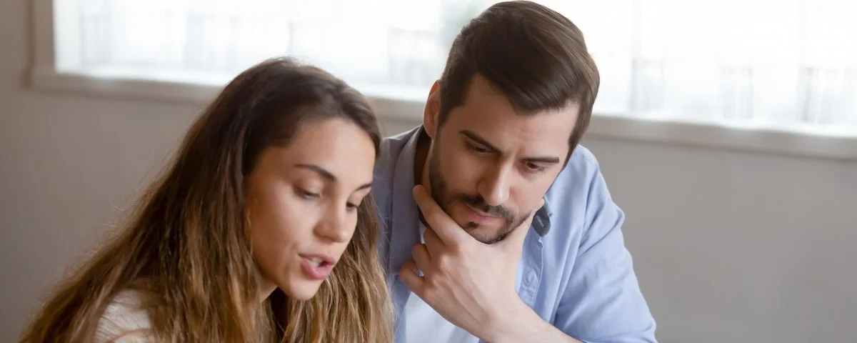 Un jeune couple multiethnique pensif paie des factures en ligne sur un ordinateur portable et lit une correspondance ou un document papier. 