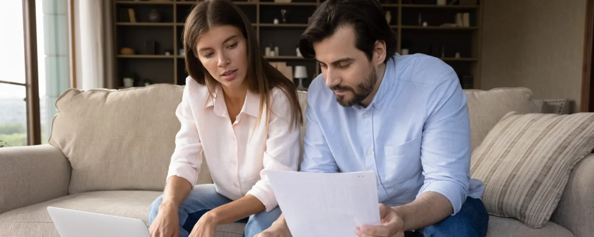 Jeune couple familial concentré calculant les dépenses, analysant les factures bancaires, gérant le budget mensuel, planifiant les investissements, payant les services en ligne à l'aide d'une application informatique.