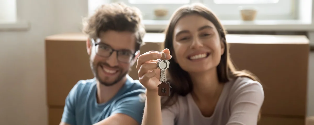 Jeune couple heureux montrant les clés de sa nouvelle maison, regardant la caméra, souriant, assis devant des cartons de déménagement, se sentant heureux, appréciant le déménagement dans un nouvel appartement, une nouvelle maison.