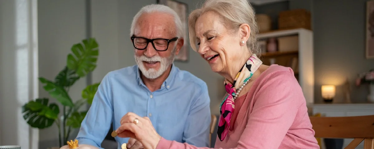 Couple de retraités joyeux assis à une table, mettant des pièces dans une tirelire