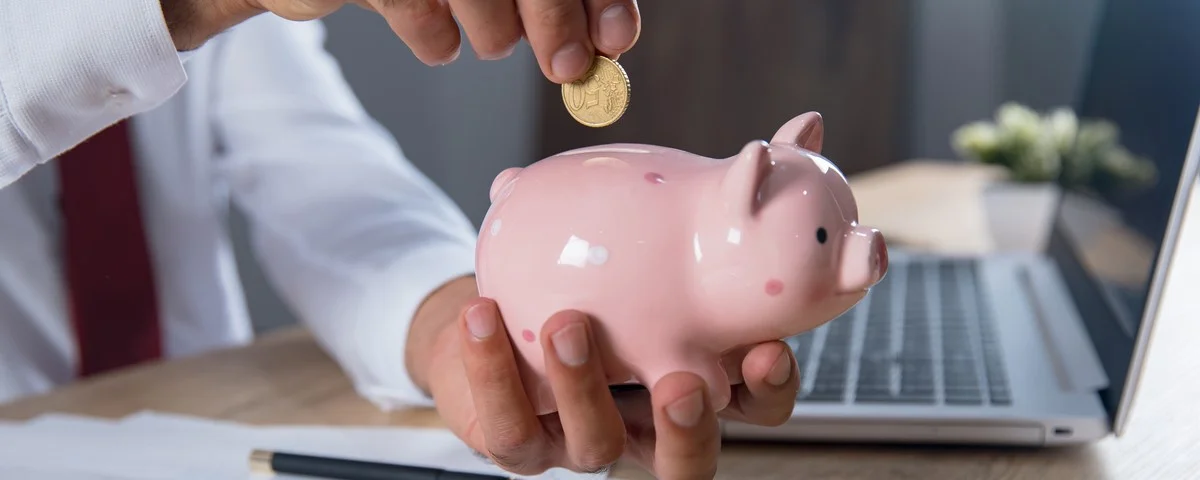 Homme tenant une pièce de monnaie avec une tirelire et un ordinateur sur une table.