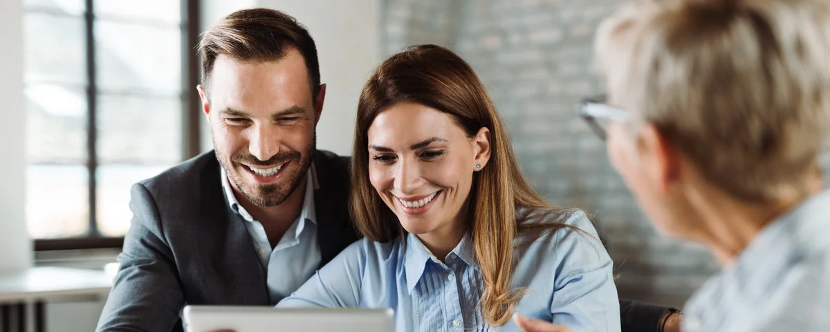 Couple heureux utilisant la tablette tactile lors d'une réunion avec leur agent d'assurance au bureau.