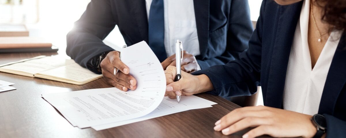  Un avocat, ses mains et un contrat, en compagnie d'une équipe commerciale, assis à un bureau dans un bureau, en train de signer des documents.